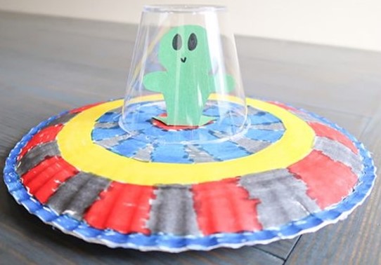 Completed craft featuring paper plate "UFO" with a clear plastic cup as the cockpit and a paper alien inside.